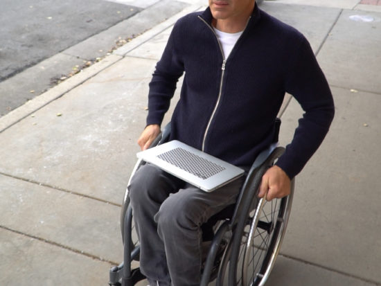Man in wheelchair on sidewalk with laptop and CatTongue Phat Cat Tablet Grip